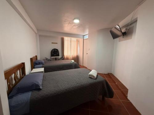 a room with three beds and a tv on the wall at Hostal La Reserva - Pisco in Pisco
