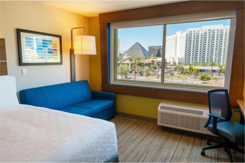 ラスベガスにあるHoliday Inn Express & Suites - Las Vegas - E Tropicana by IHGのベッドと青いソファと窓のあるホテルの部屋
