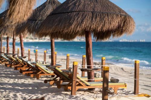 a row of straw umbrellas and chairs on a beach at Club Regina Cancun in Cancún