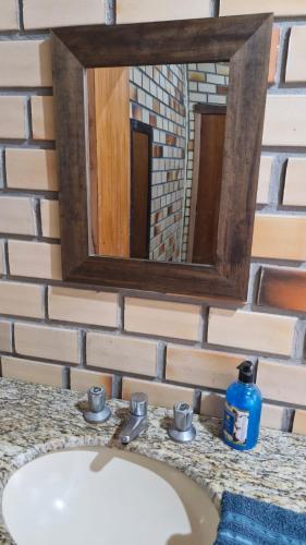 a bathroom sink with a mirror on a brick wall at Família SOL & LUA Guarda do Embaú SC in Guarda do Embaú