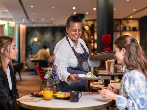 Ein Mann serviert zwei Frauen Essen in einem Restaurant in der Unterkunft Sofitel Brussels Europe in Brüssel
