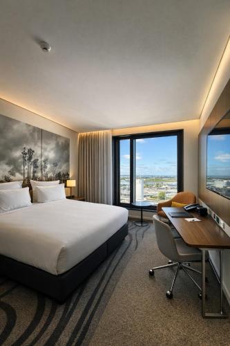a hotel room with a bed and a desk and window at Novotel Christchurch Airport in Christchurch