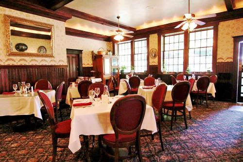 uma sala de jantar com mesas e cadeiras com toalha de mesa branca em The National Hotel em Jamestown