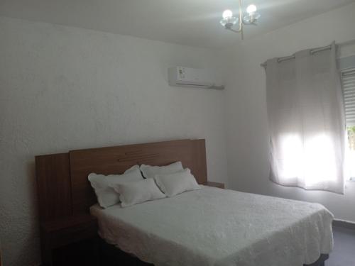 a bedroom with a bed with white sheets and a window at Casa de verano 2 in Piriápolis