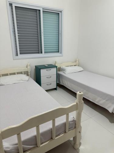 two beds in a white room with a window at Chalés Brisa Do Mar in São Sebastião