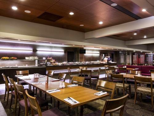 リバプールにあるメルキュール シドニー リバプールの木製のテーブルと椅子、キッチンを備えたレストラン