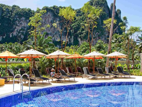a pool with chairs and umbrellas next to a resort at ibis Styles Krabi Ao Nang in Ao Nang Beach