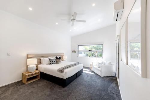 Un dormitorio blanco con una cama y una silla. en Sleek Stylish Family Beach House Near Junction, en Noosa Heads