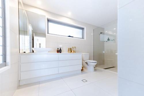 Un baño blanco con lavabo e inodoro. en Sleek Stylish Family Beach House Near Junction, en Noosa Heads