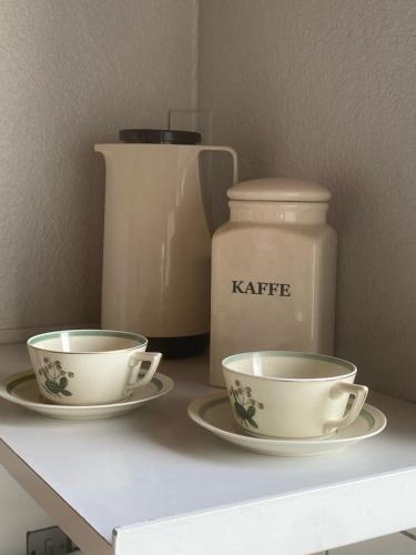 two cups and plates on a shelf with a kettle at Møgeltønder BB in Tønder