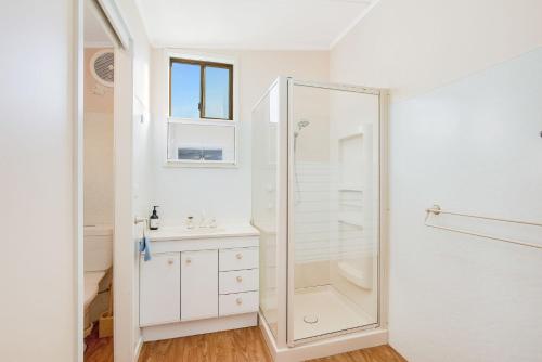 een witte badkamer met douche en wastafel bij 3 Barragoot Street in Bermagui