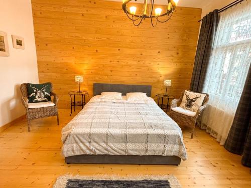 een slaapkamer met een bed en 2 stoelen en een kroonluchter bij Willa Maciejówka Historyczny Dom Góralski przy Równi Krupowej in Zakopane