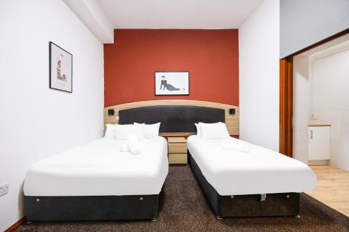 two beds in a room with a red wall at Arinza Hotel, London Ilford in Ilford