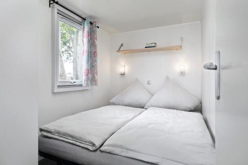 un lit dans une petite pièce avec une fenêtre dans l'établissement KNAUS Campingpark Eckwarderhörne, à Eckwarderhörne
