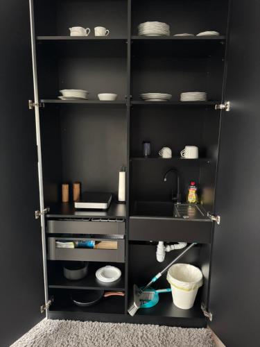a black kitchen with a shelf with dishes and a sink at Studio am Waldrand in Bad Hersfeld