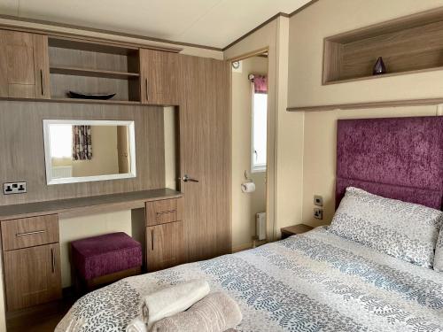 Schlafzimmer mit einem Bett mit einem lila Kopfteil und einem Spiegel in der Unterkunft Lake Front 2 Bed Caravan, South Cerney in Cirencester