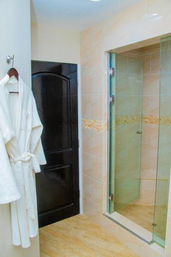 a bathroom with a shower and a white robe on a rack at Royal Ambassador Hotel in Harbel