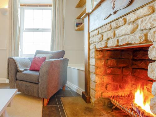 a living room with a stone fireplace and a chair at Jack's Cottage in Tinwell