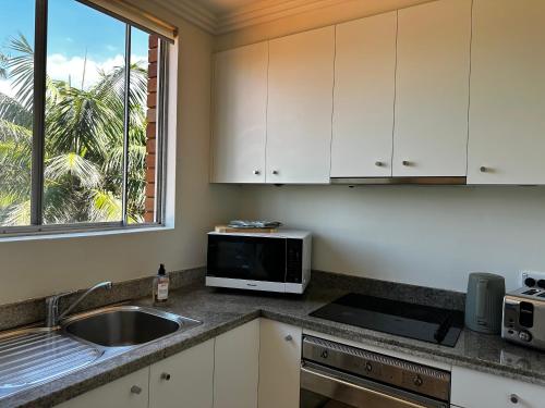 een keuken met een spoelbak en een magnetron bij Beach & Ocean View Apartments Tamarama in Sydney