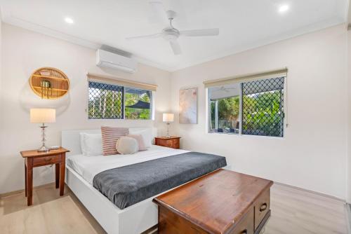 a white bedroom with a bed and two windows at Eden House Kewarra Beach in Kewarra Beach