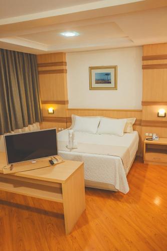 a bedroom with a bed and a desk with a computer at Grande Hotel Guarapuava in Guarapuava