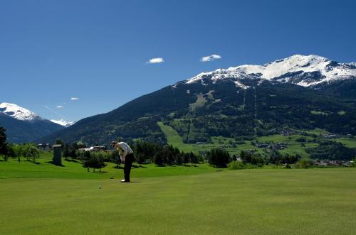 a man playing golf on a green with mountains in the background at Sottovento Luxury Hospitality in Bormio