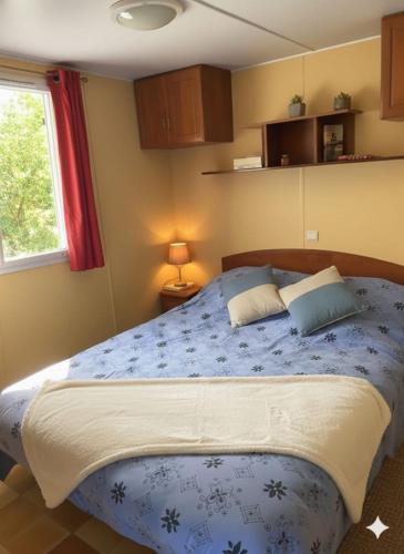 a bedroom with a bed with a blue comforter and a window at Mobil Home sans vis a vis in Saint-Georges-de-Didonne