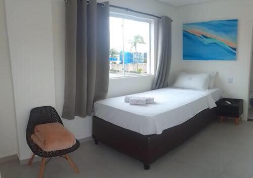 a bedroom with a bed and a window and a chair at Hotel Rosa da Ilha Guaruja - 80m do mar, 02 piscinas, sala de jogos, brinquedão de percurso para crianças in Guarujá
