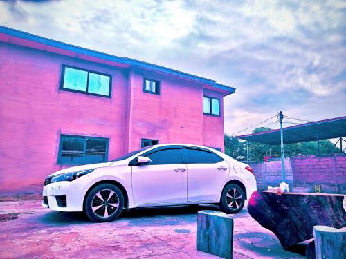 een witte auto geparkeerd voor een roze gebouw bij huazhi in Accra