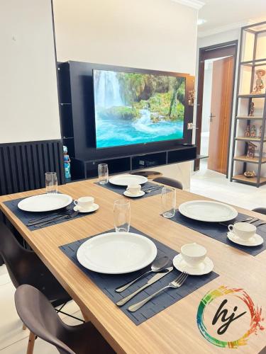 een grote houten tafel met borden en een tv bij Atria 304 in Tambaú