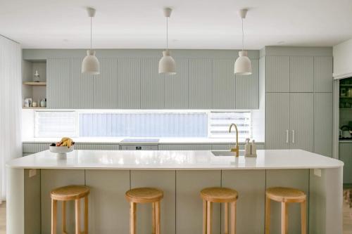 a kitchen with a large white island with stools at Bundeena Bungalow in Bundeena
