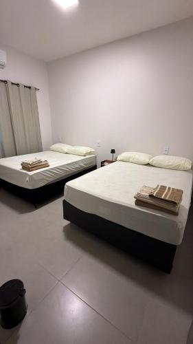 two beds in a white room with towels on them at Casa aconchegante com 02 quartos climatizados in Nova Mutum