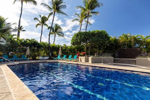 a swimming pool with blue chairs and palm trees at Peaceful condo with lanai & beach essentials in Waikoloa