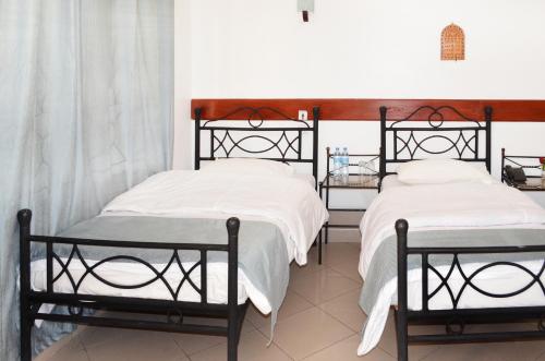 two twin beds in a room with white sheets at Arusha Naaz Hotel in Arusha