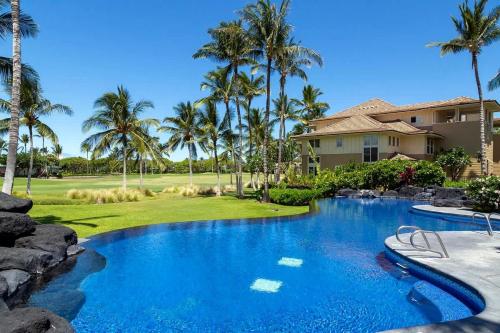 a swimming pool in front of a house with palm trees at Spacious 2BR condo with lanai & pool in Waikoloa