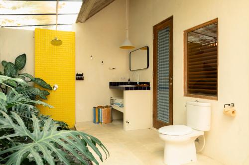 a bathroom with a toilet and a yellow wall at Shelter Island in Ubud
