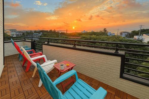 a balcony with chairs and a table with a sunset at Maeda Reaf Resotプライベートビーチまで徒歩3分 in Onna