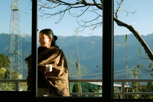 a woman standing in a window with a cup of coffee at Aavya backpackers hostel in Tawang