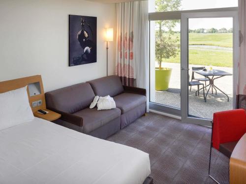 a hotel room with a bed and a couch and a table at Novotel Saint-Quentin en Yvelines in Magny-les-Hameaux