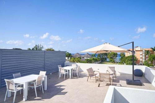 een terras met tafels, stoelen en een parasol bij Coral Beach 204 - by ZenBreak in Saint Peter