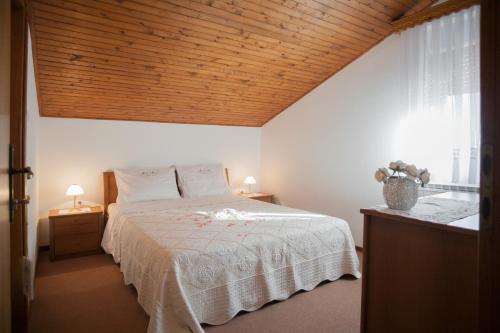 a bedroom with a white bed with a wooden ceiling at Janezinovi House in Ratečevo Brdo