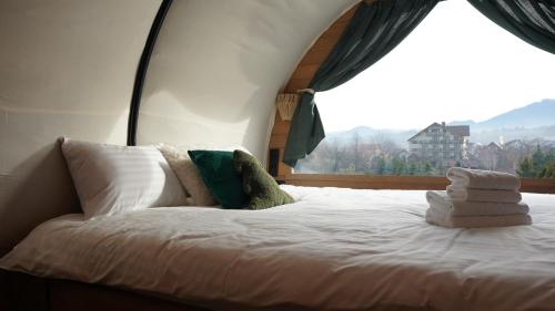 un letto con lenzuola e cuscini bianchi di fronte a una finestra di Nomad by Hora cu Brazi a Zărneşti