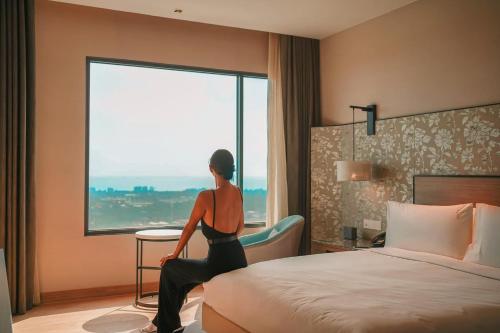 a woman sitting on a bed looking out of a window at Holiday Inn & Suites Rayong City Centre by IHG in Rayong