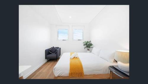 a white bedroom with a bed with a yellow blanket at Modern Studio in Burwood in Sydney