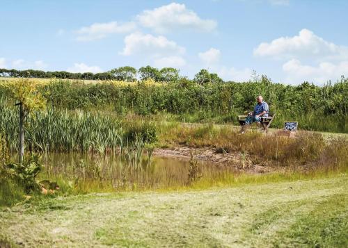a man sitting on a bench next to a pond at Holderness Country Park in Tunstall