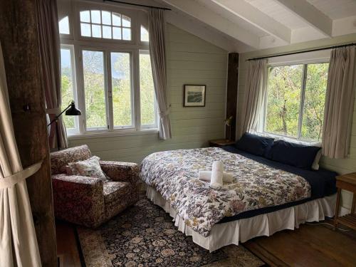 a bedroom with a bed and a chair and windows at Leura Haven Rustic Mountain Cottage in Leura