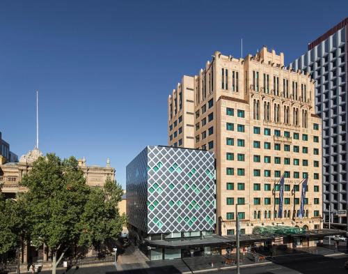 a tall building with a glass facade in a city at Mayfair Hotel Adelaide by IHG in Adelaide