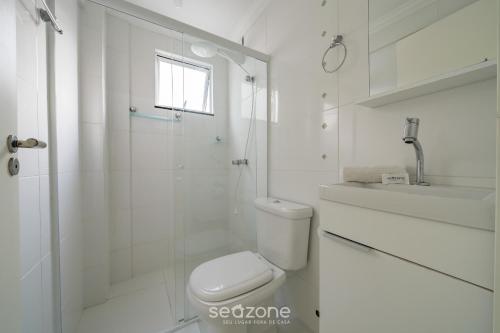 ein weißes Badezimmer mit Toilette und Dusche in der Unterkunft Apto 2Q c/ churrasq. no centro - Bombinhas CAA103 in Bombinhas