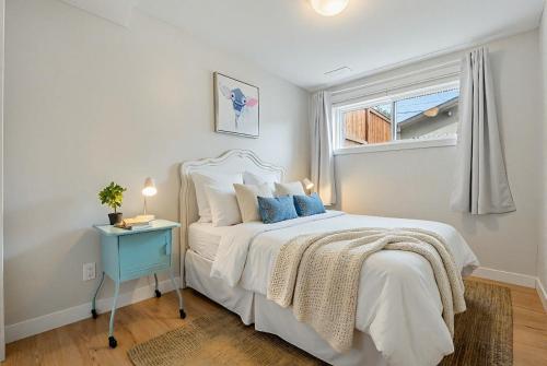 a white bedroom with a bed and a window at Cozy and Welcoming 2BR Basement Suite In The Heart of Calgary in Calgary