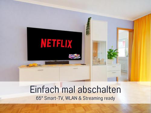 ein Wohnzimmer mit einem Fernseher an der Wand in der Unterkunft Stadtdomizil Ziegelfeld - Ruhig & Zentral, 65" TV, Südbalkon, vollausgestattete Küche, Altstadt fußläufig, Bahnhof 5-10 Min, Tiefgarage im Haus, in Waldshut-Tiengen
